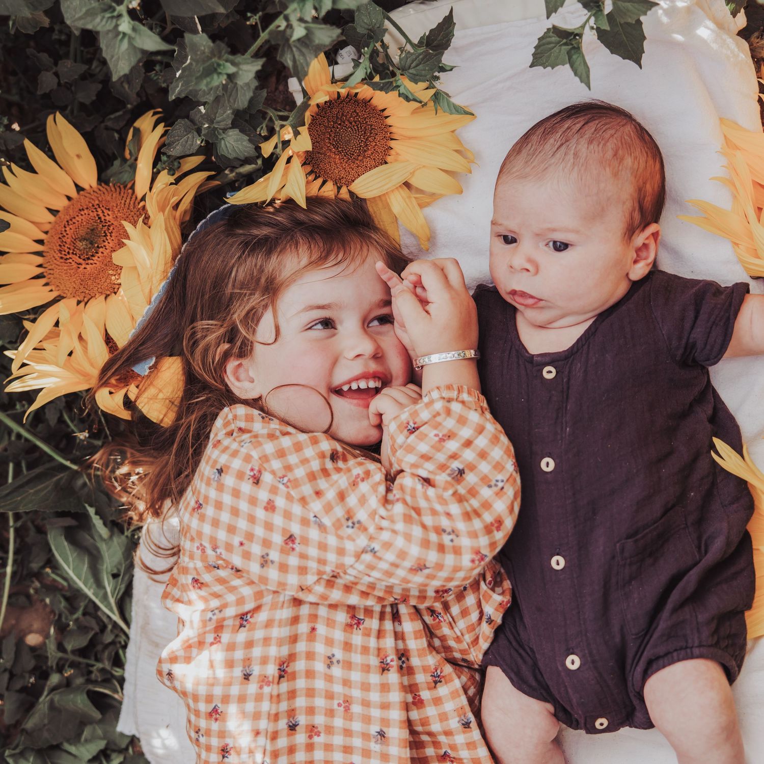 Two siblings lying together surrounded by sunflowers during a natural family photoshoot.
