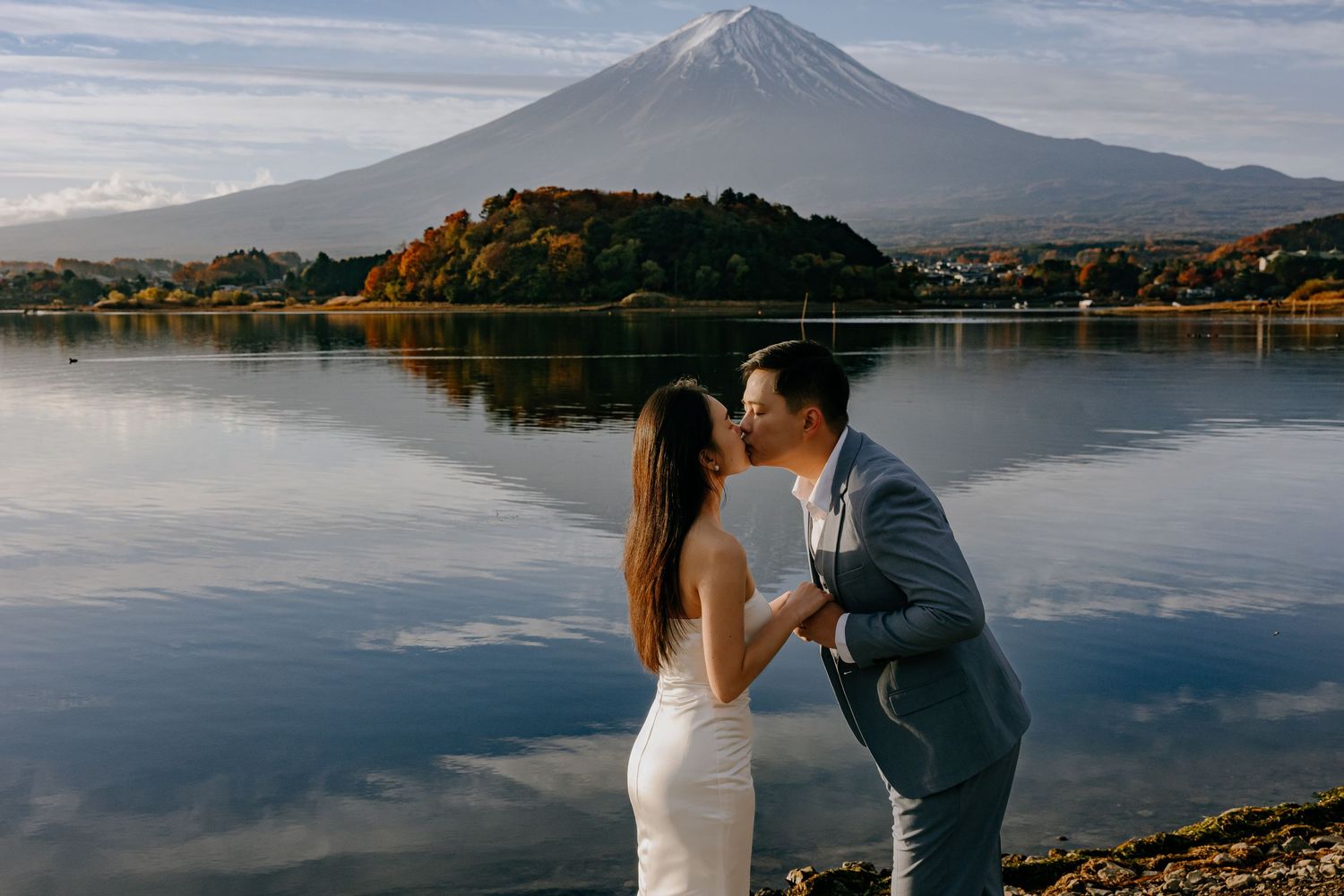Wedding couple embraces by scenic Lake Kawaguchiko with majestic Mount Fuji in the background during sunset.