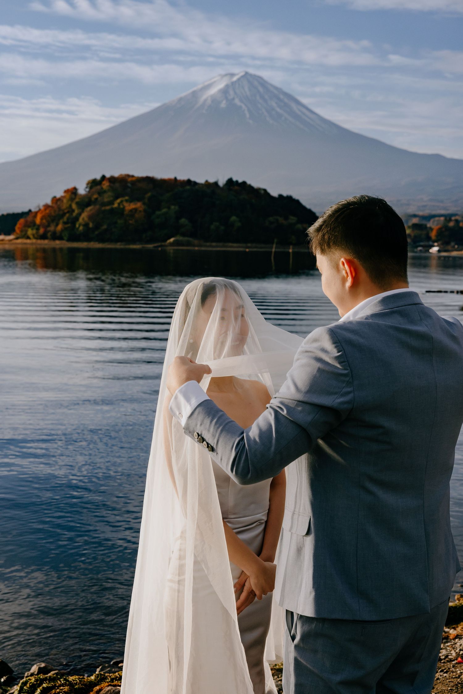 A couple in wedding attire admires Mount Fuji while standing by Lake Kawaguchiko in Japan.