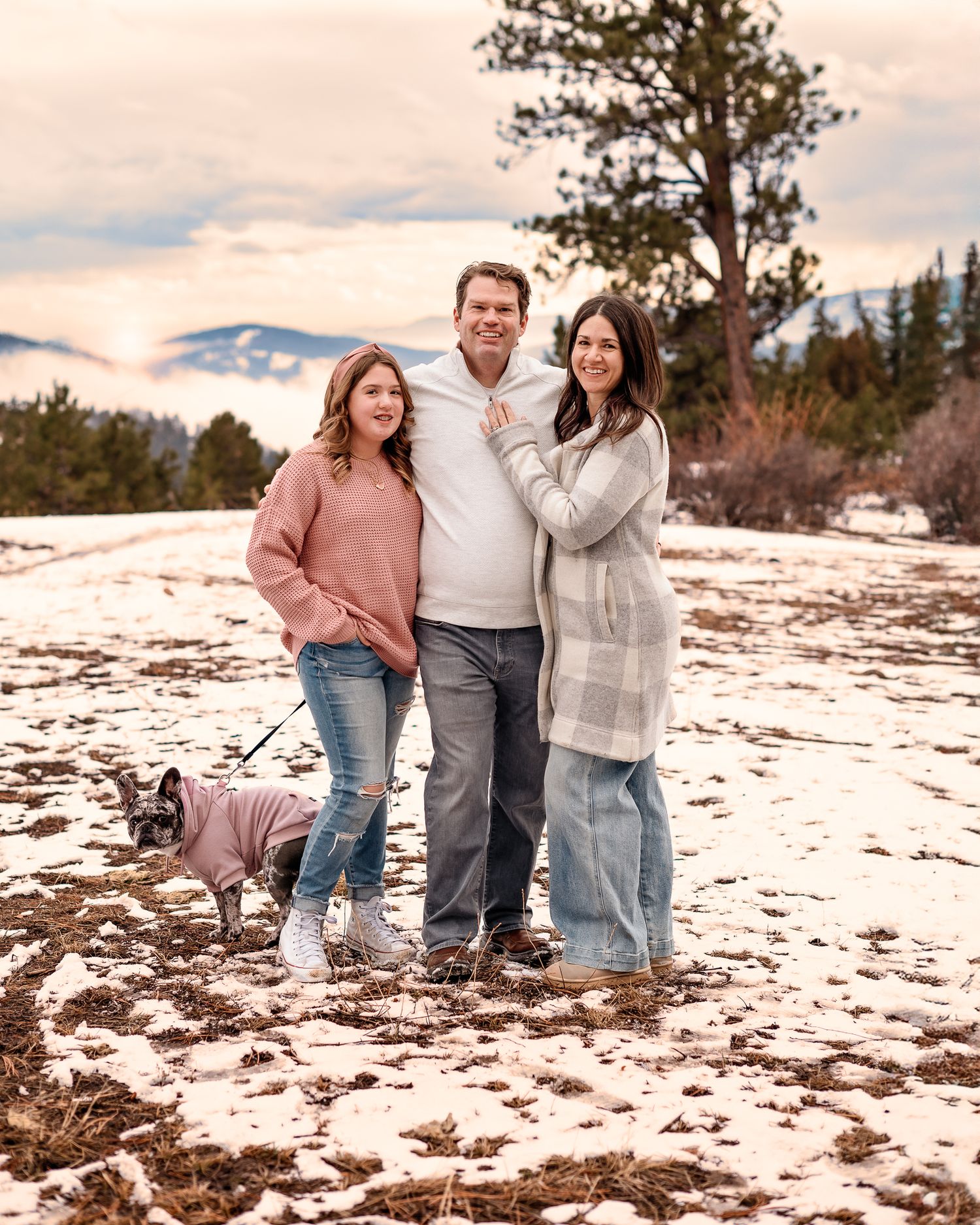 a mom, dad, and tween girl smiling at the camera from a snowy Conifer mountain