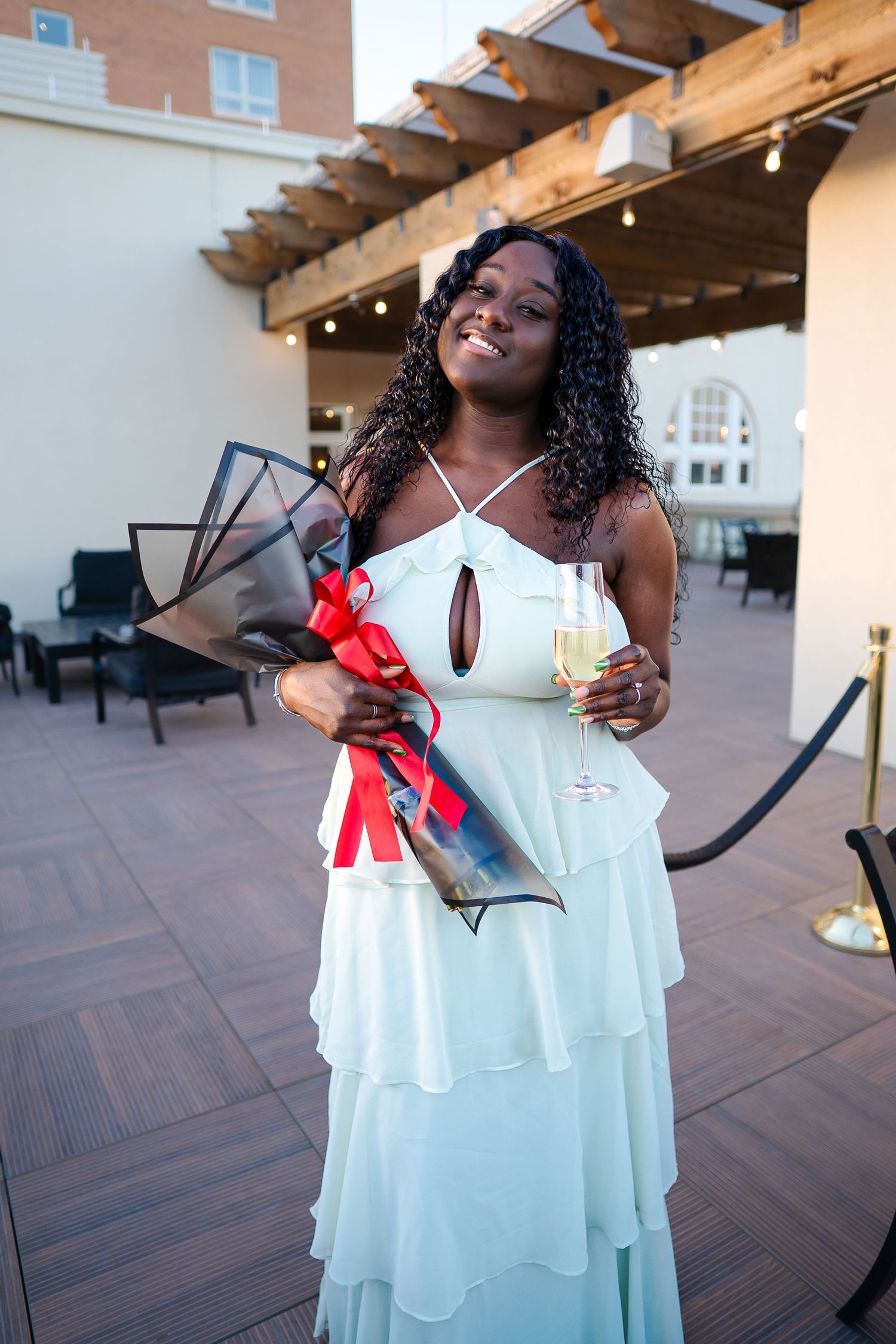 A person in a flowing white dress poses joyfully on a rooftop terrace with wooden beams overhead.