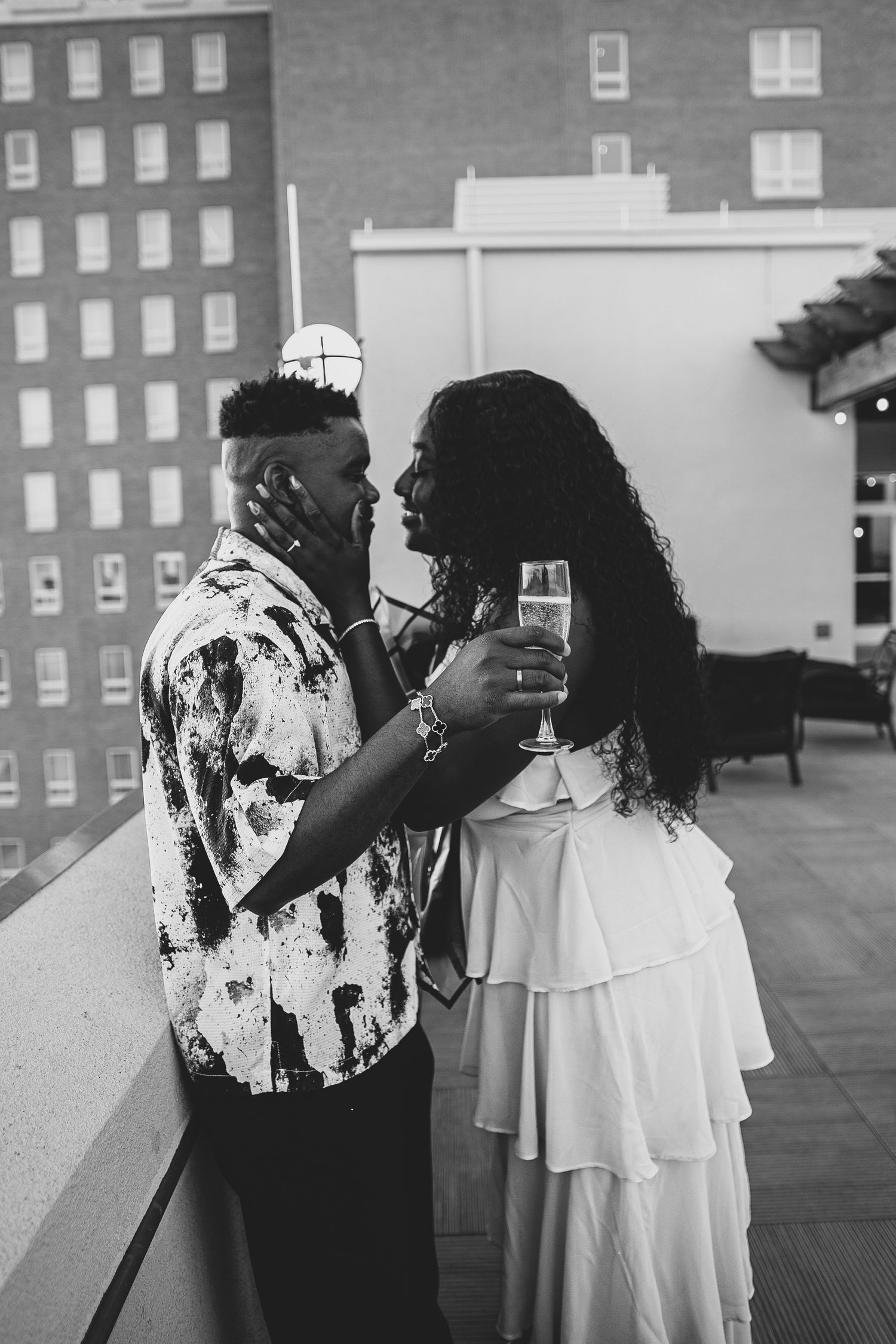 A romantic black and white photo of a couple sharing an intimate moment on a rooftop terrace with drinks.
