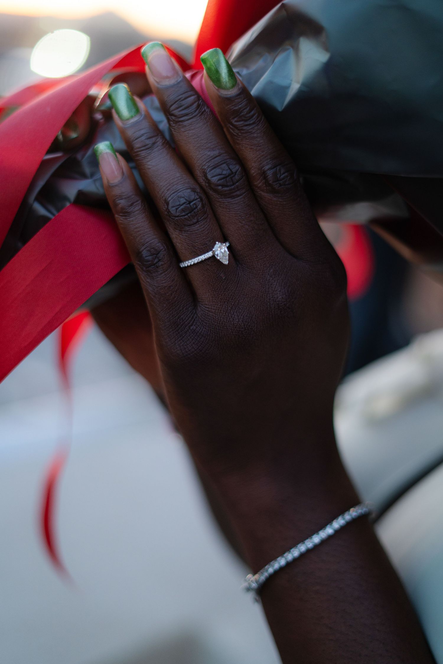 Close-up of hands wearing sparkling diamond engagement rings against a red and black background.