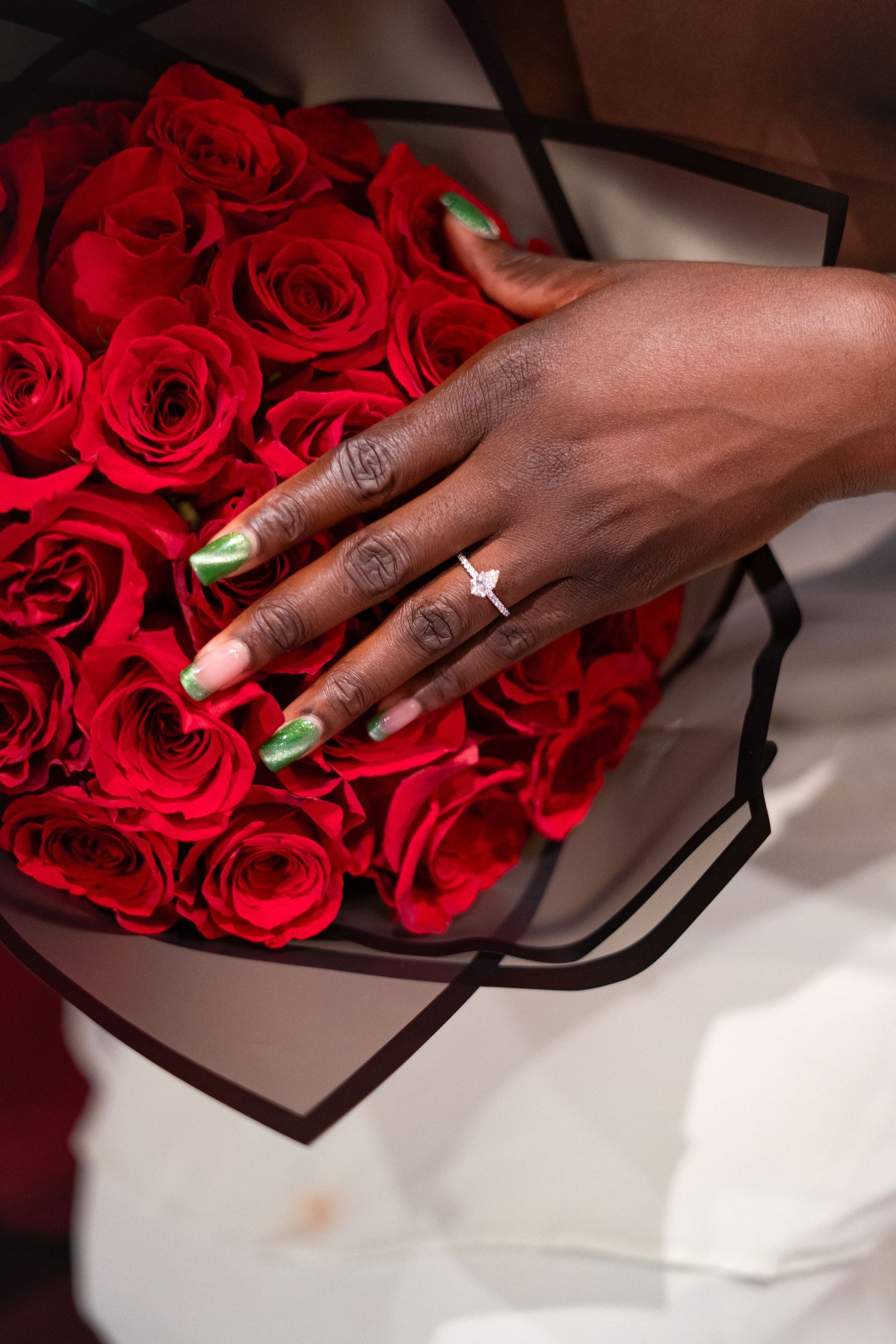 Close-up of hands arranging vibrant red roses in an elegant dark wooden box against a white surface.