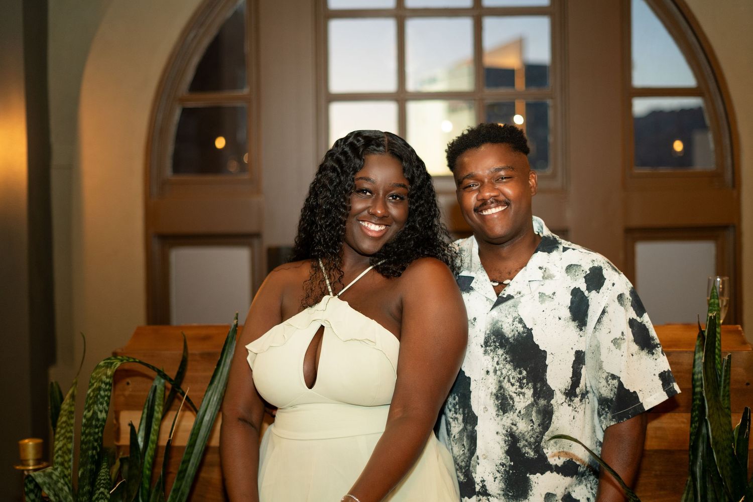 Wedding party members in black and white floral attire pose together at an elegant indoor venue.