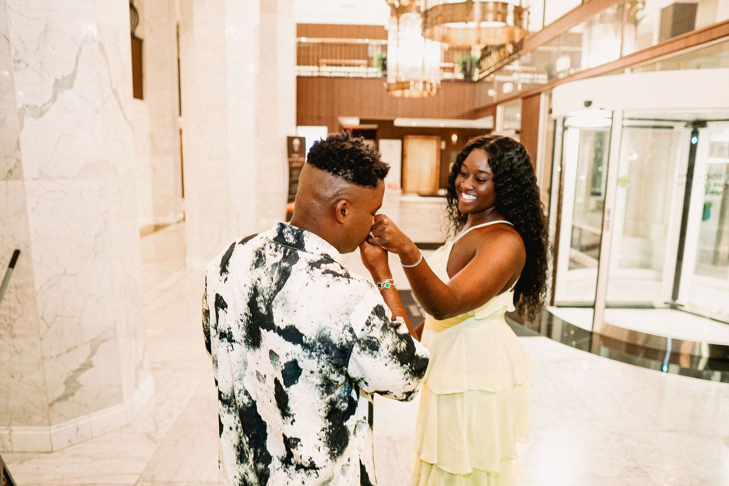 A couple shares a romantic moment in an elegant indoor setting with marble columns and warm lighting.