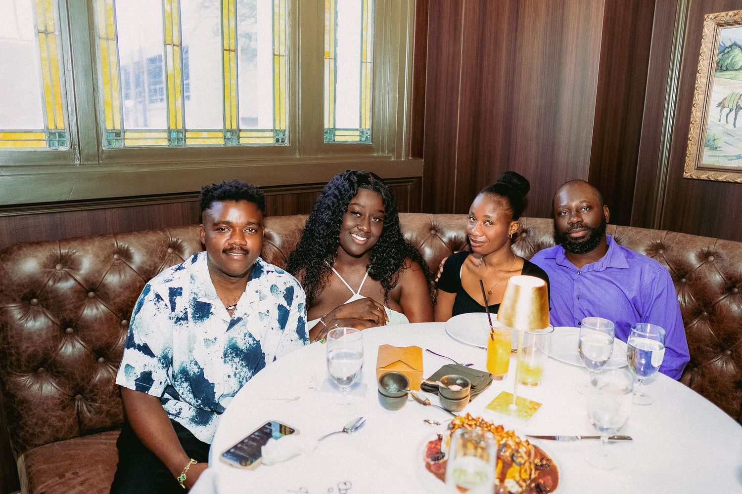 Group of friends enjoying dinner and drinks together at a restaurant booth with leather seating.