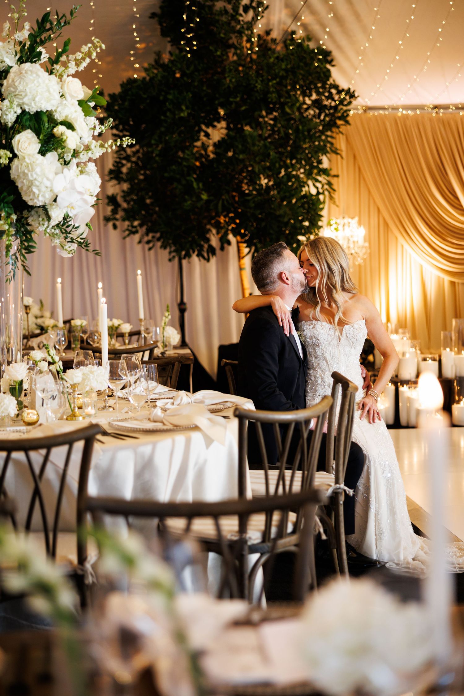 Elegant wedding reception venue with white floral centerpieces, draped fabric, and romantic ambient lighting.