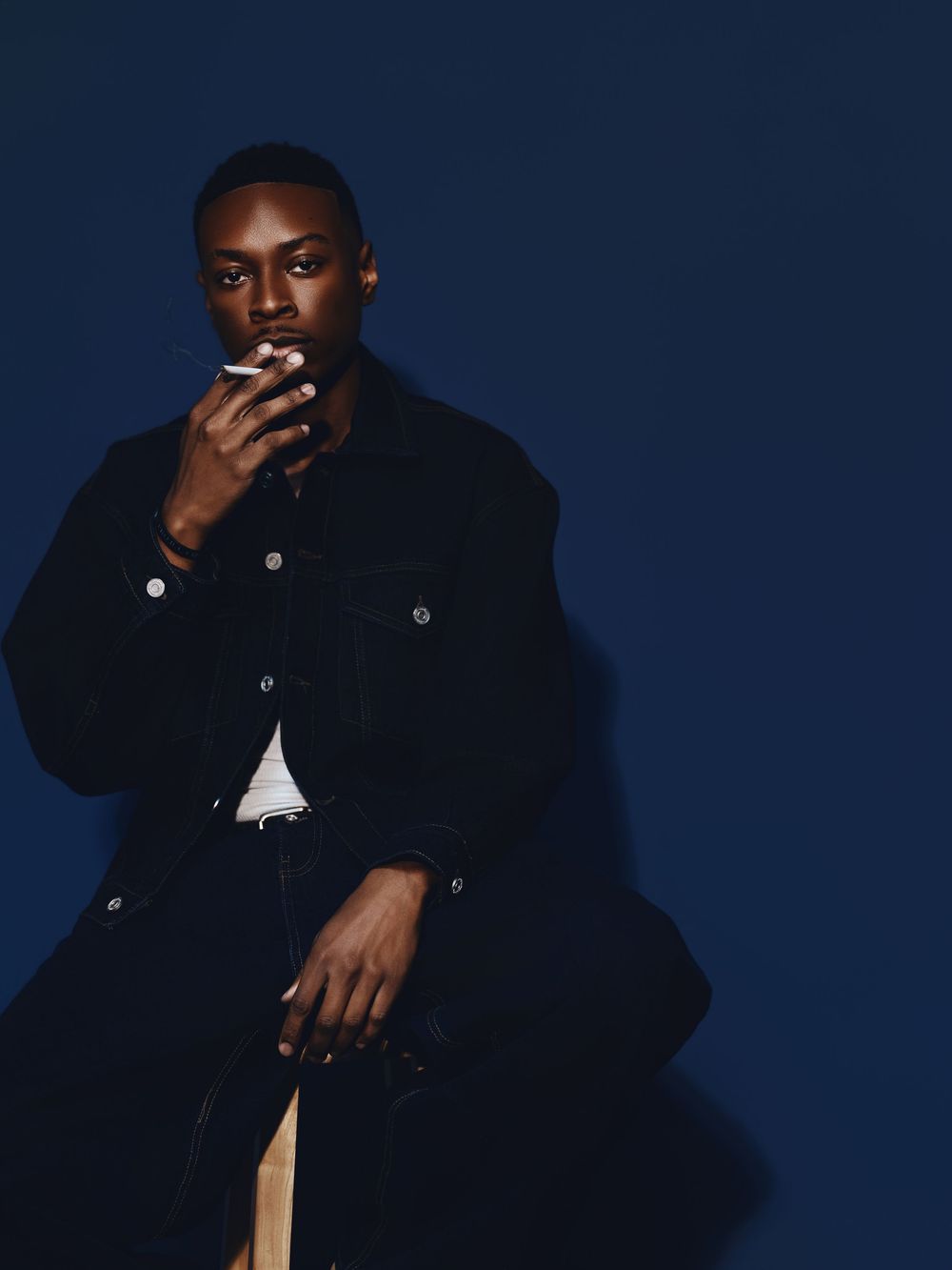 Artistic portrait against dark blue background showing person in black jacket with contemplative pose.