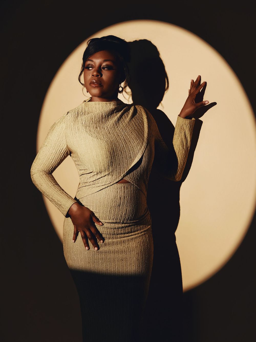A dramatic series of silhouetted poses against a circular spotlight showing movement in a cream sweater.