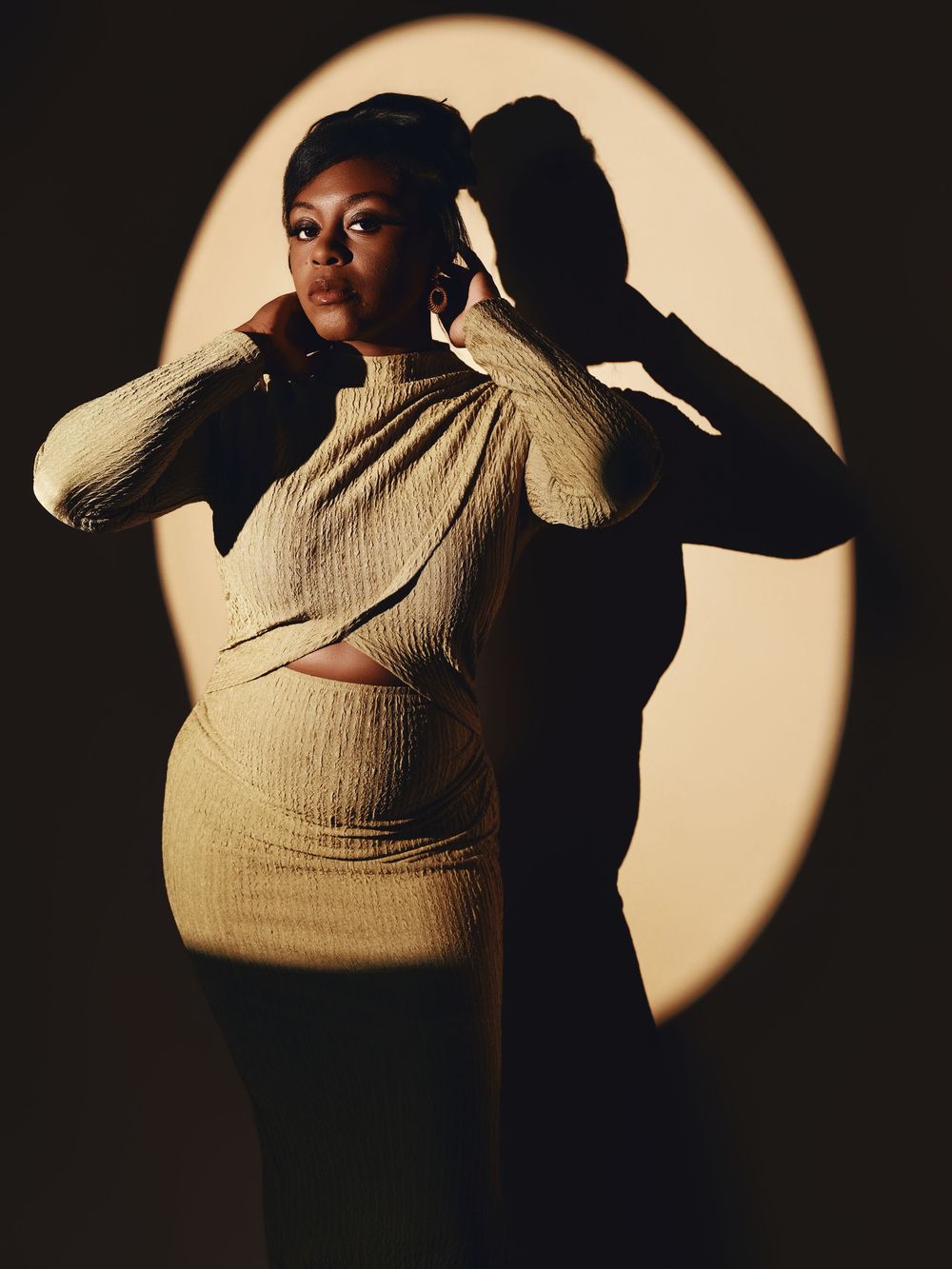 A dramatic silhouette series against a circular light shows a figure in a ribbed sweater posing expressively in darkness.