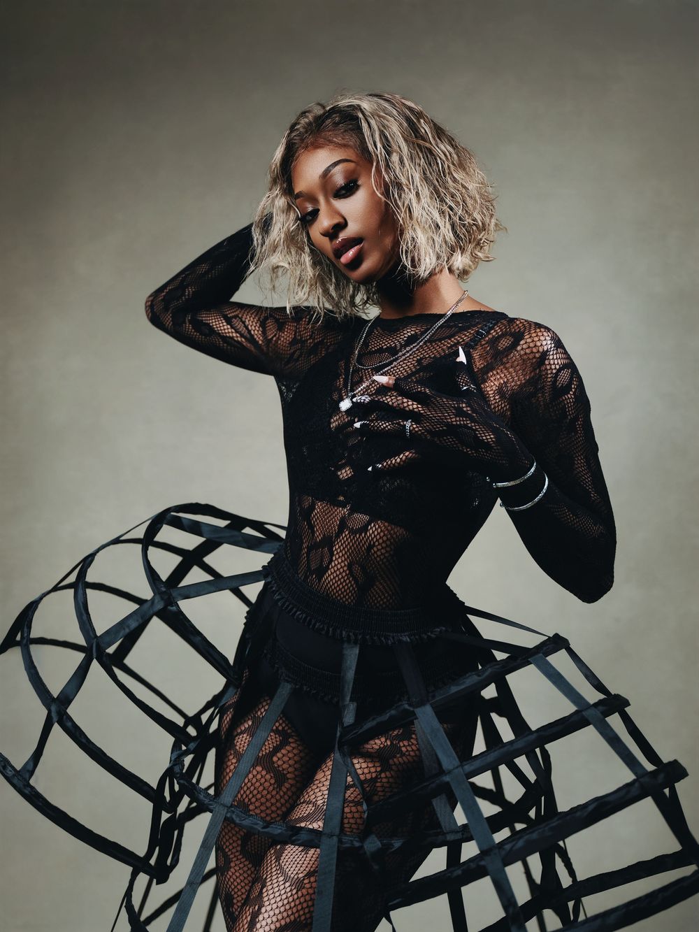 Model in sheer black mesh outfit with structured hoop skirt strikes elegant pose in studio.