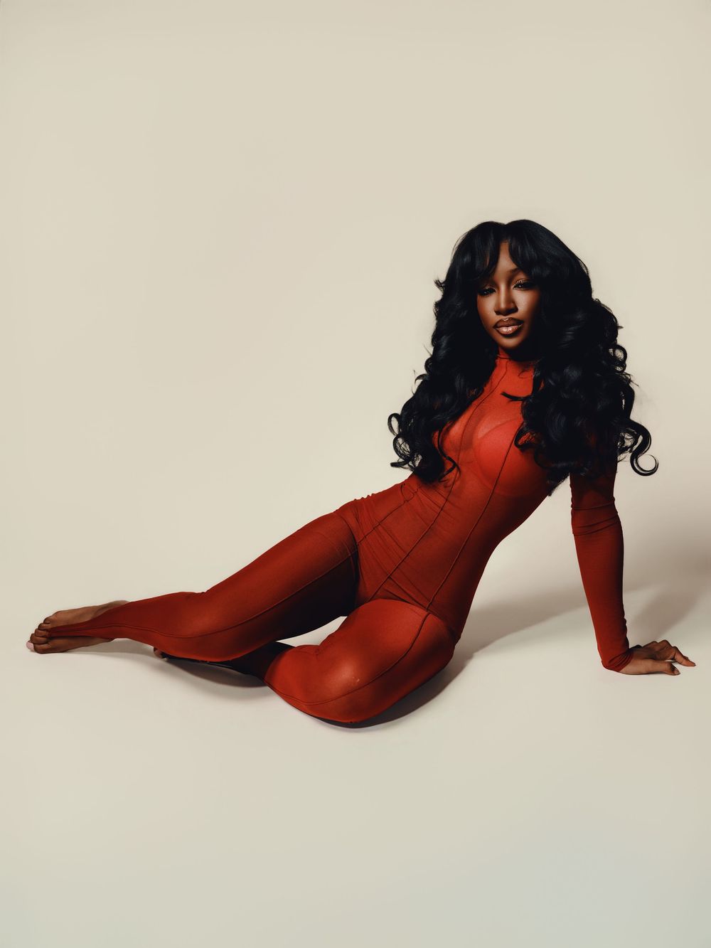 Model in red long-sleeved bodysuit poses gracefully against neutral backdrop in artistic fashion series.