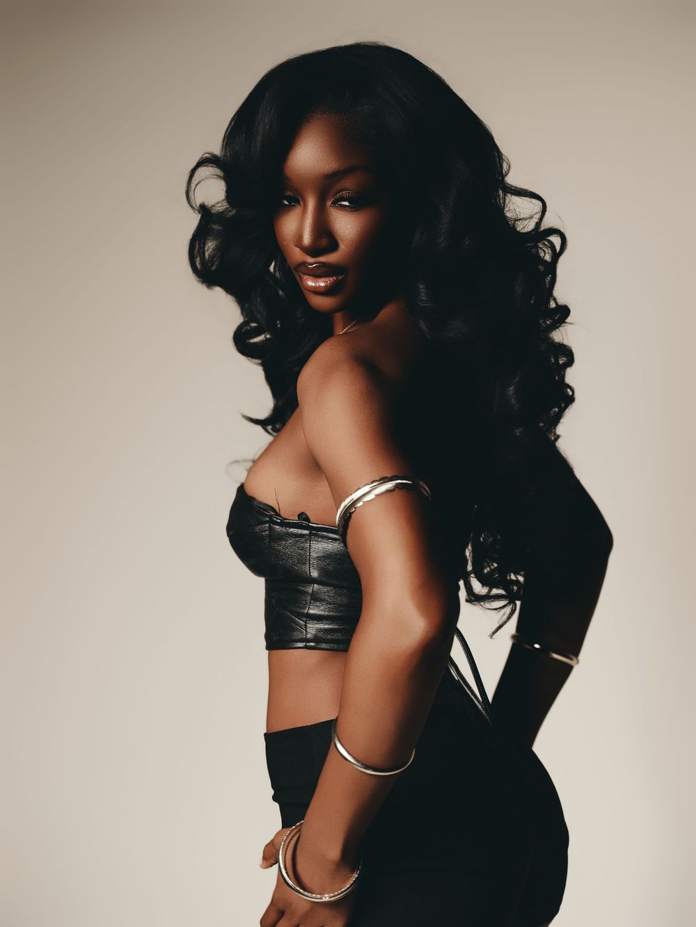 A series of glamour portraits featuring a model in a black corset with dramatic lighting and voluminous dark curls.