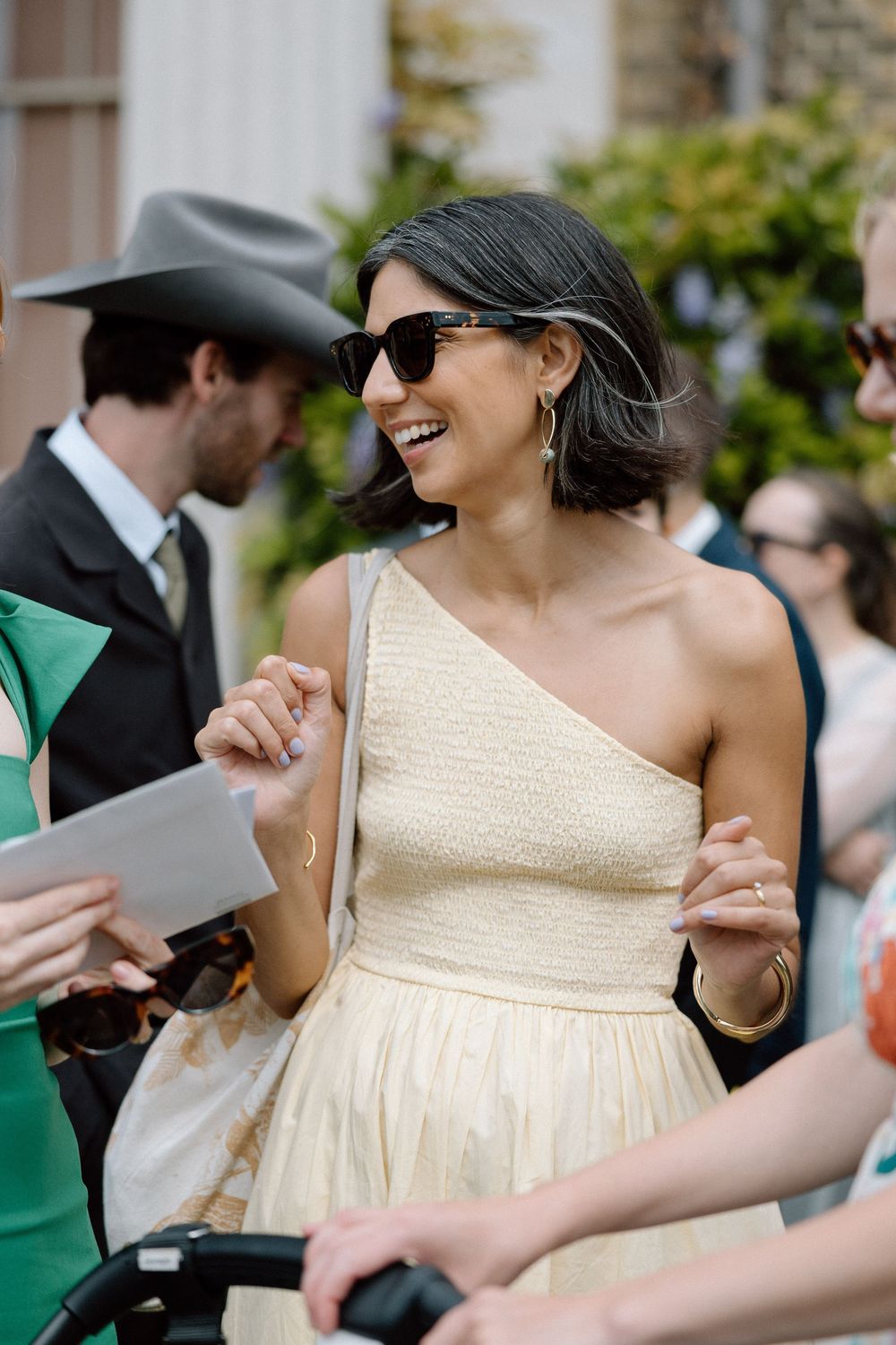 Wedding guests in formal attire sharing laughs during an outdoor celebration.