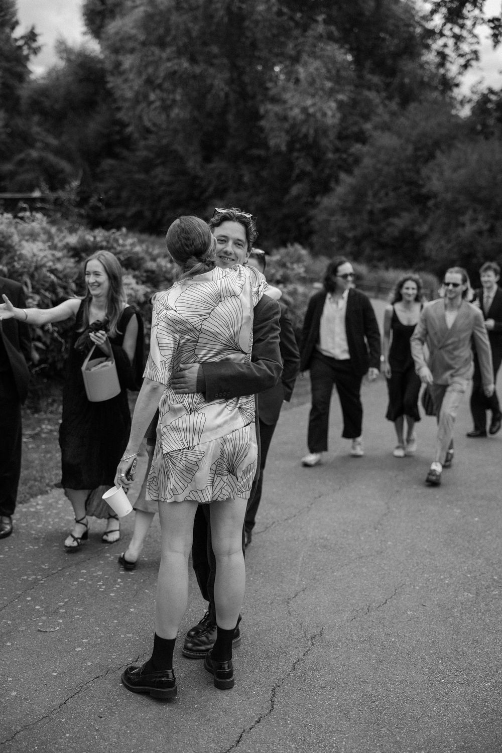Wedding party walking and dancing playfully on a paved outdoor path.