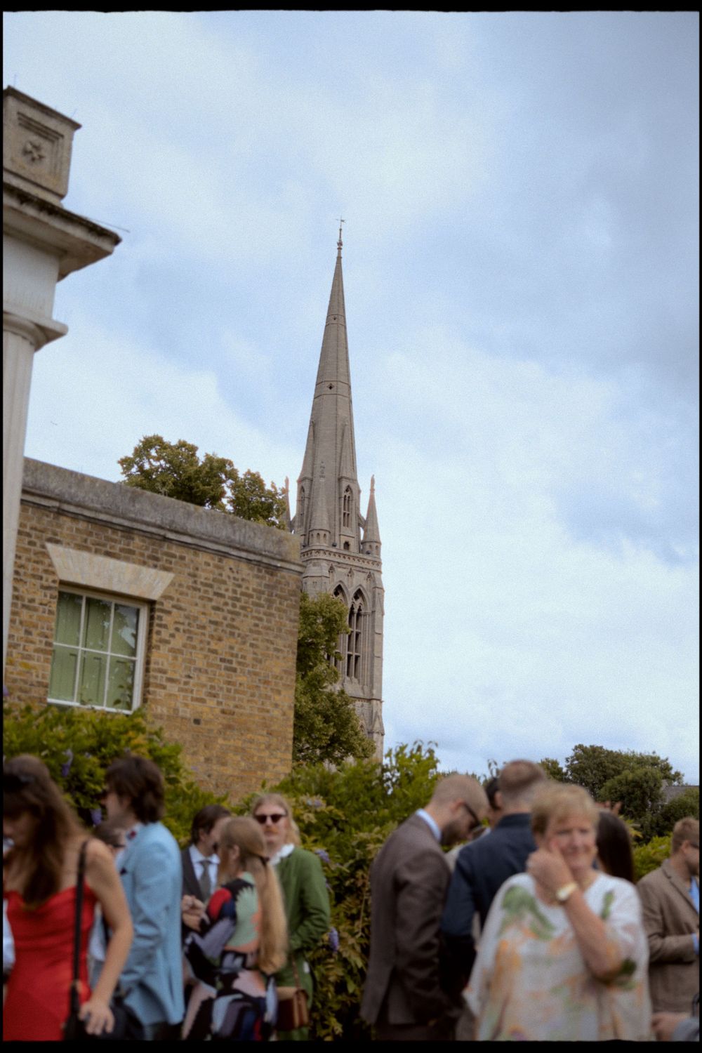 Church spire visible in background as wedding guests gather outside.