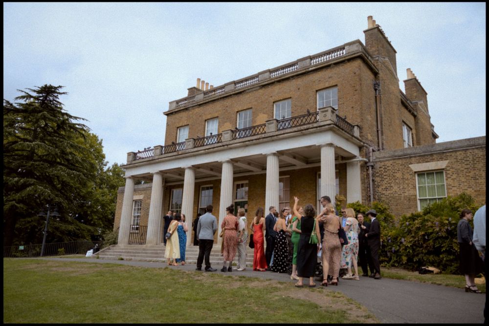 Elegant stone building with columned entrance where wedding guests are mingling at Clissold House.