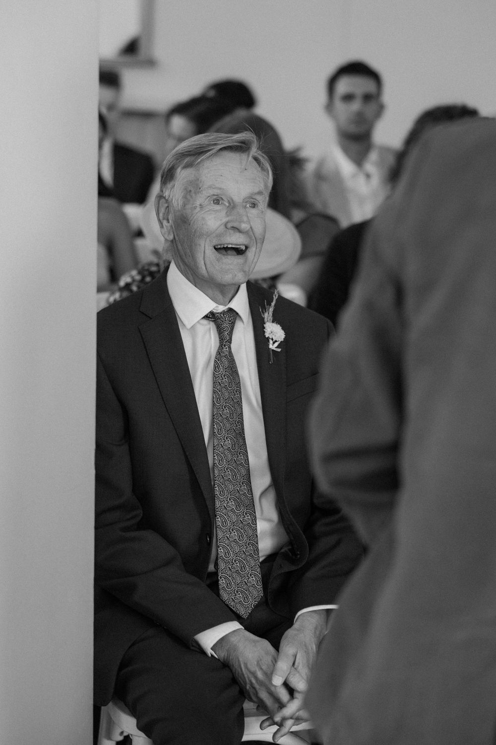 Guest at formal event laughing heartily while seated during celebration.