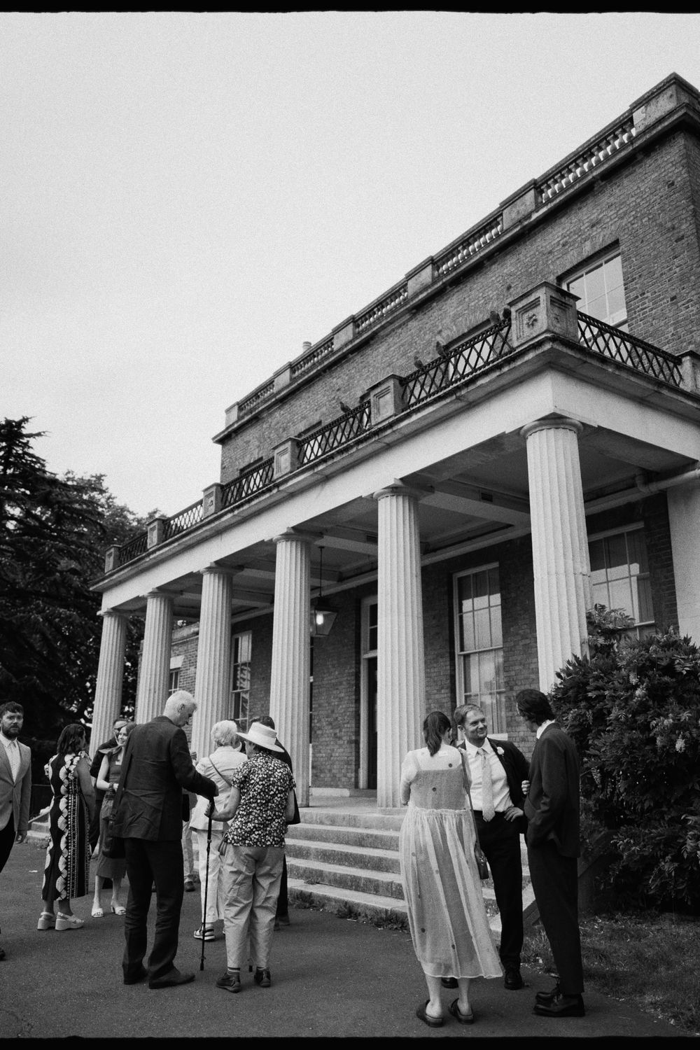 Classical building exterior with white columns and brick facade where guests are gathering.