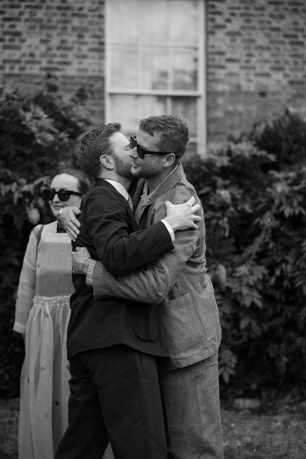Wedding guests sharing emotional embraces in a garden setting.