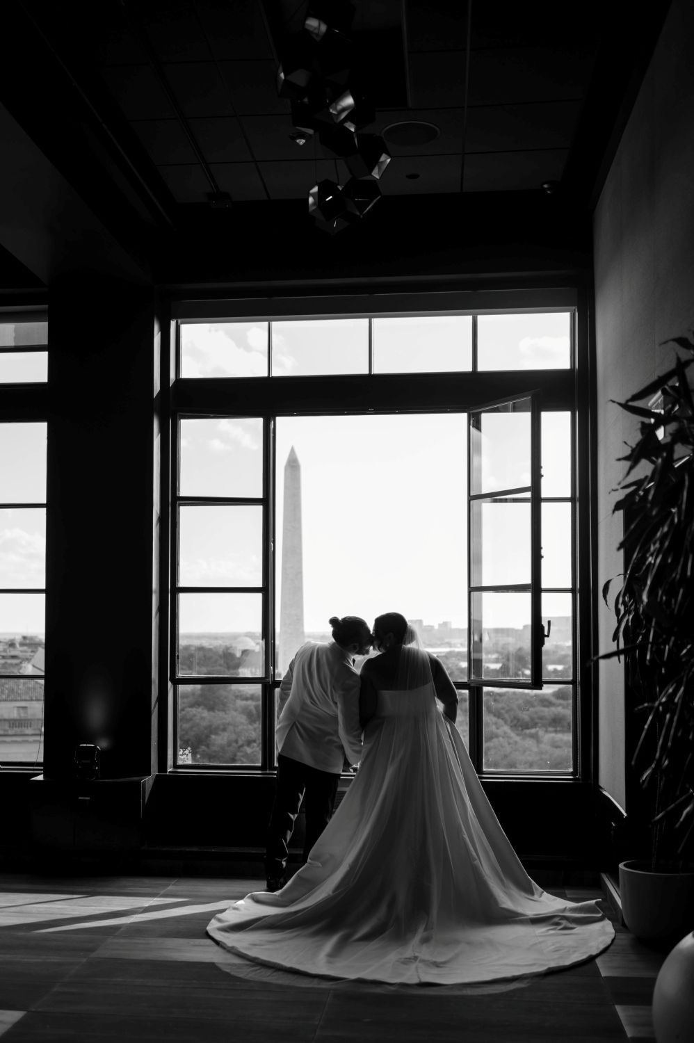 A romantic silhouette of a couple by a window overlooking the Washington Monument, with a flowing wedding dress train.