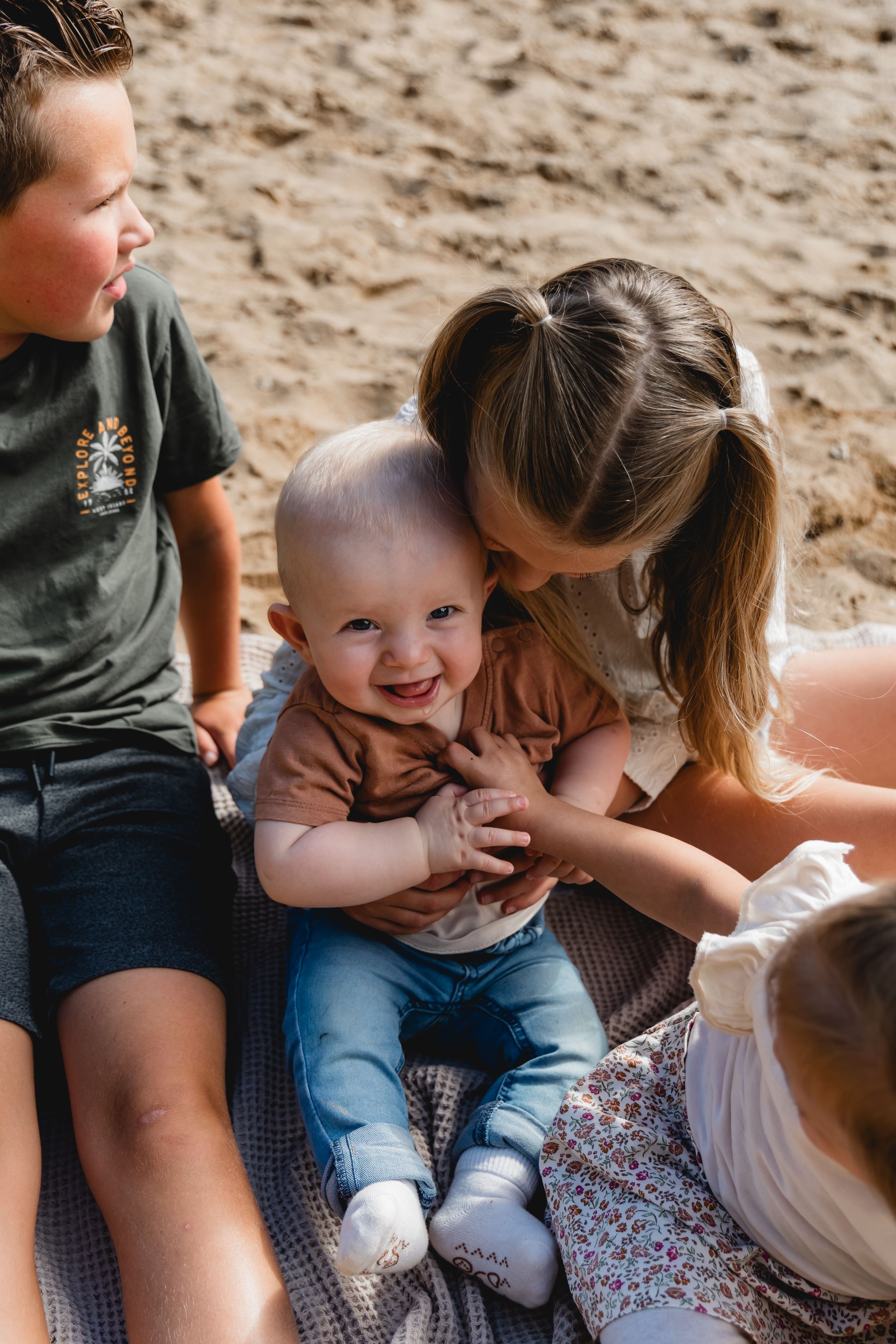 Candid moment of laughter and cuddles shared on a picnic blanket at the beach.