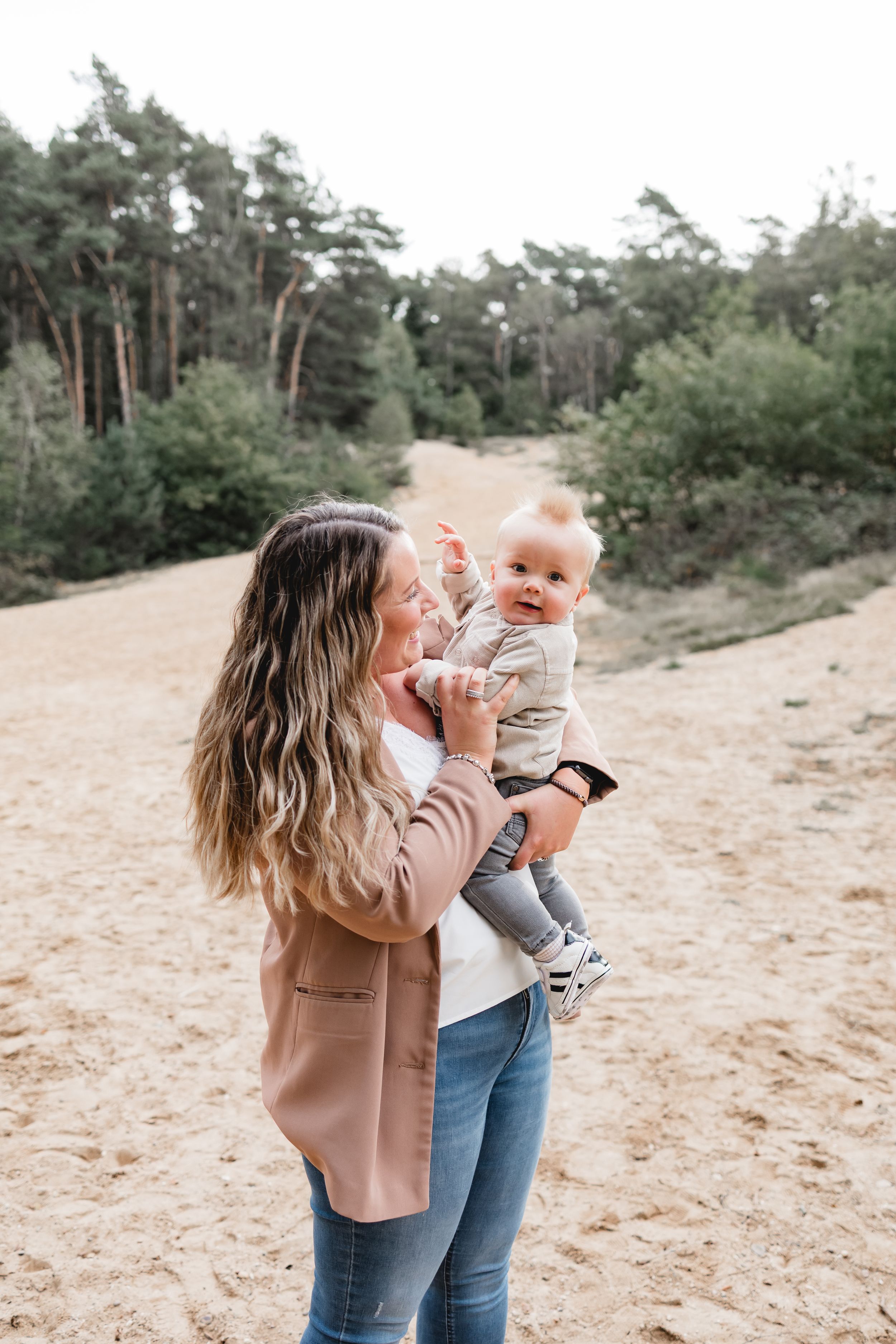 Playful interaction between parent and child against a backdrop of pine trees on sandy terrain.