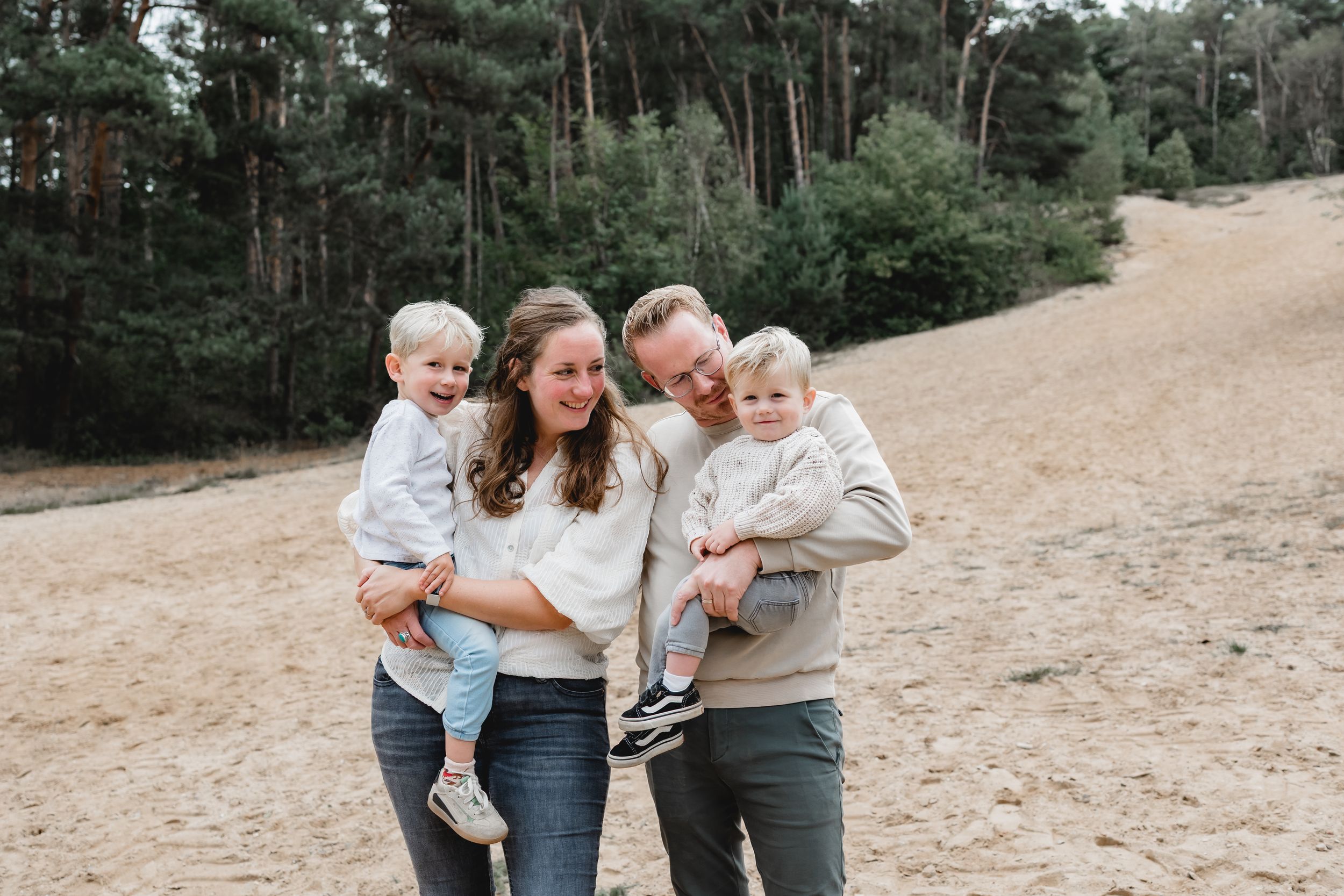 Family walking together on a sandy path surrounded by pine trees on a cloudy day.