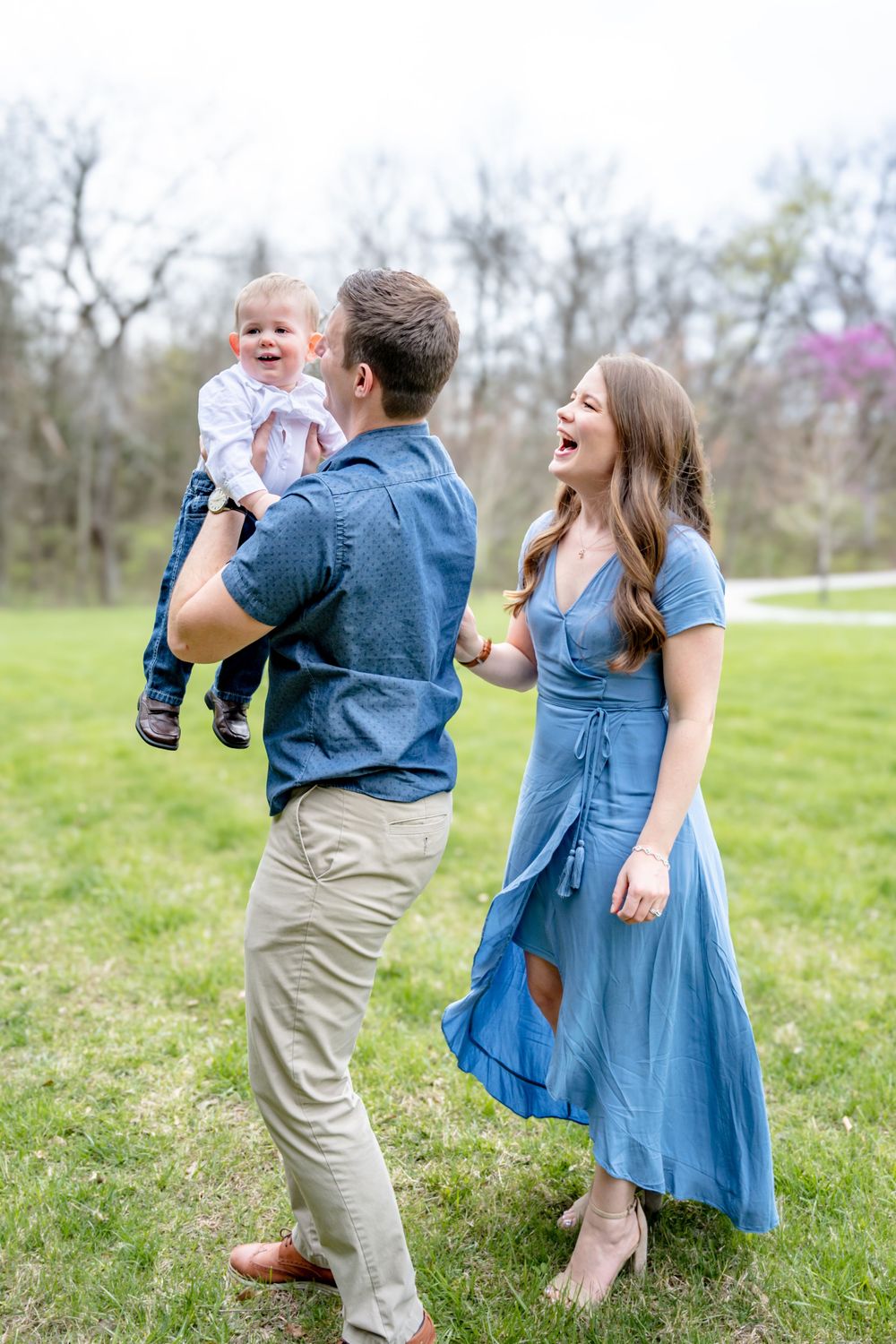 A family in coordinating denim and khaki outfits shares joyful moments together on a grassy field during a photo session.