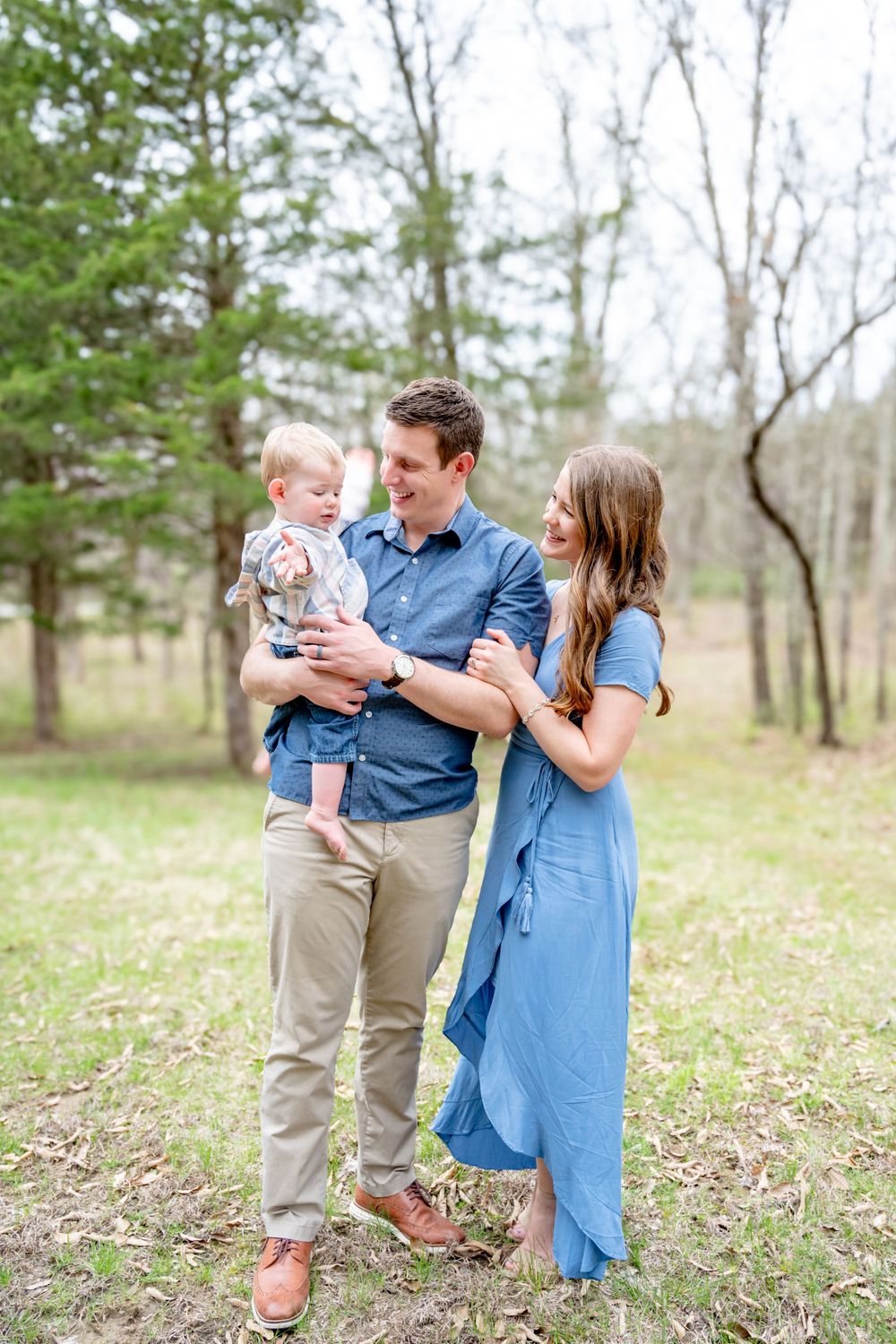 A family in coordinating blue and khaki outfits shares joyful moments together in a sunlit field with spring flowers.
