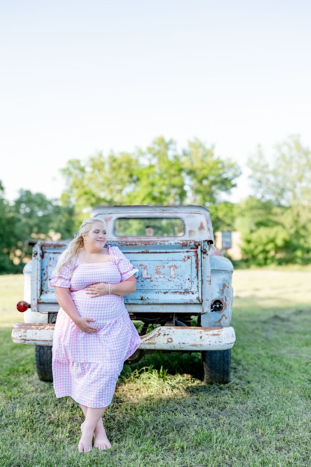 A rustic vintage turquoise pickup truck serves as a backdrop for maternity photos in a sunny meadow.