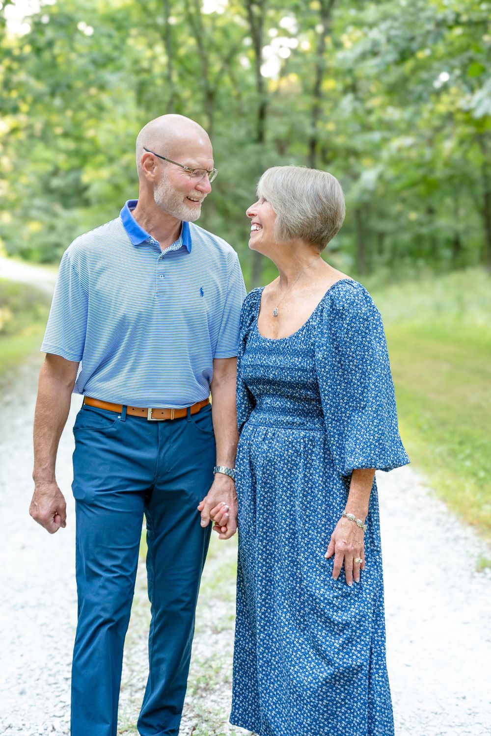 A couple shares a joyful moment while walking hand in hand on a gravel path in a wooded setting.
