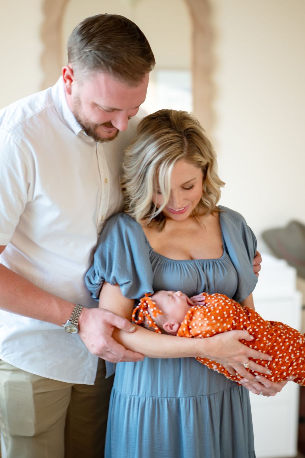 A series of tender moments between parents and their newborn baby, featuring a blue dress and orange polka dot swaddle.