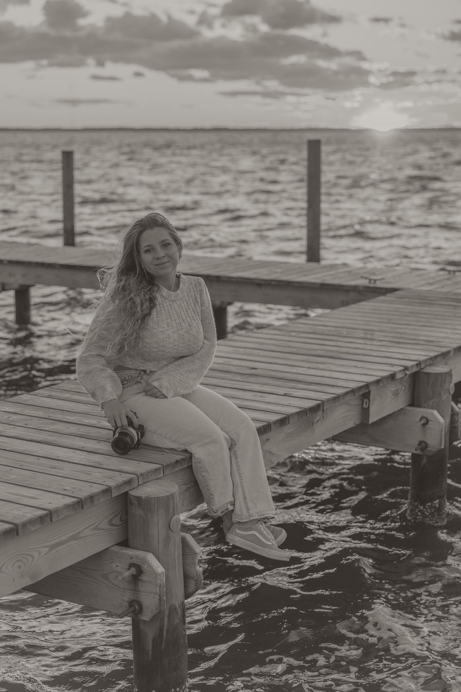 A series of black and white photos showing someone sitting on a wooden dock at sunset over a rippling ocean.