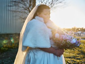 A romantic couple embraces in golden sunlight while holding a bouquet of purple wildflowers in a natural outdoor setting.