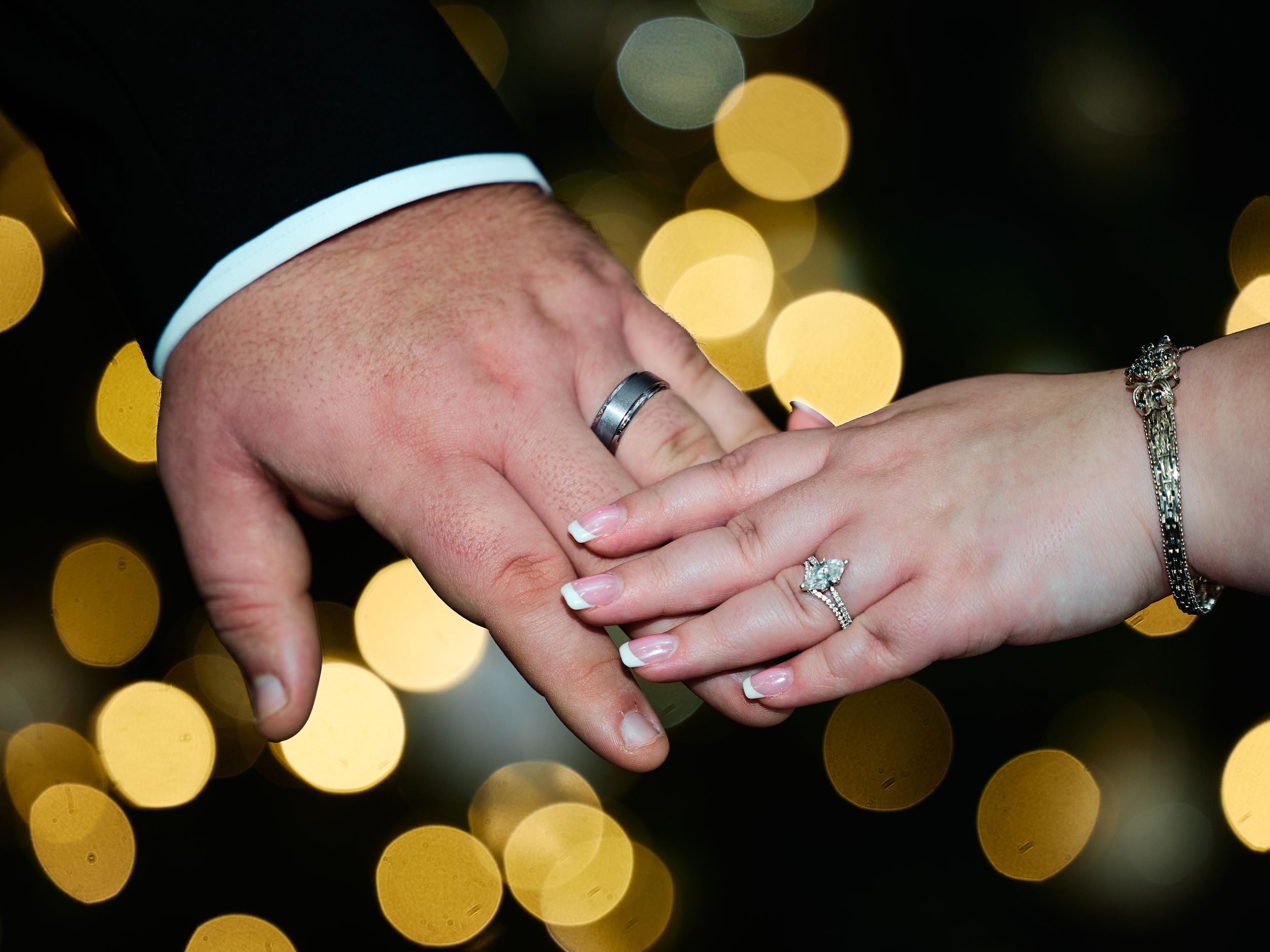 Close-up shot of hands exchanging rings during a wedding ceremony with soft bokeh lights in the background.