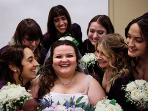 A group of bridesmaids in dark dresses share a joyful moment with the bride at a wedding celebration.