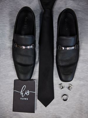 Black leather dress shoes and accessories including a tie, cufflinks, and a gift box arranged on a gray surface.