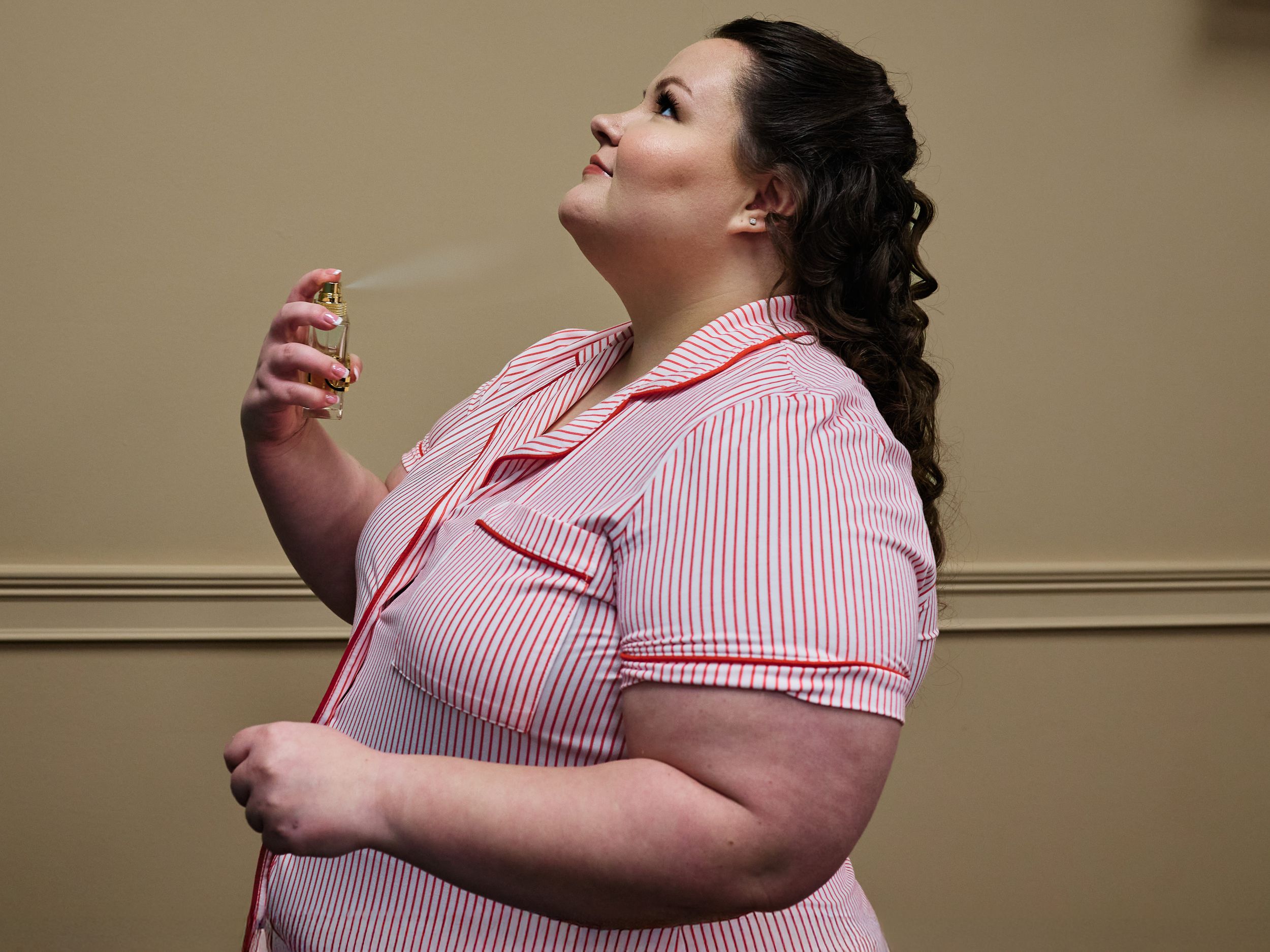 A person wearing a pink and white striped shirt stands in profile against a beige wall.