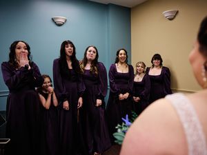 Wedding party members in dark purple dresses share candid moments while getting ready for the ceremony.