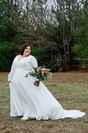 A bride in a flowing white wedding gown poses gracefully on the grass in an outdoor garden setting.