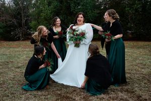 A group in formal attire including emerald green dresses and a white wedding gown pose together outdoors.