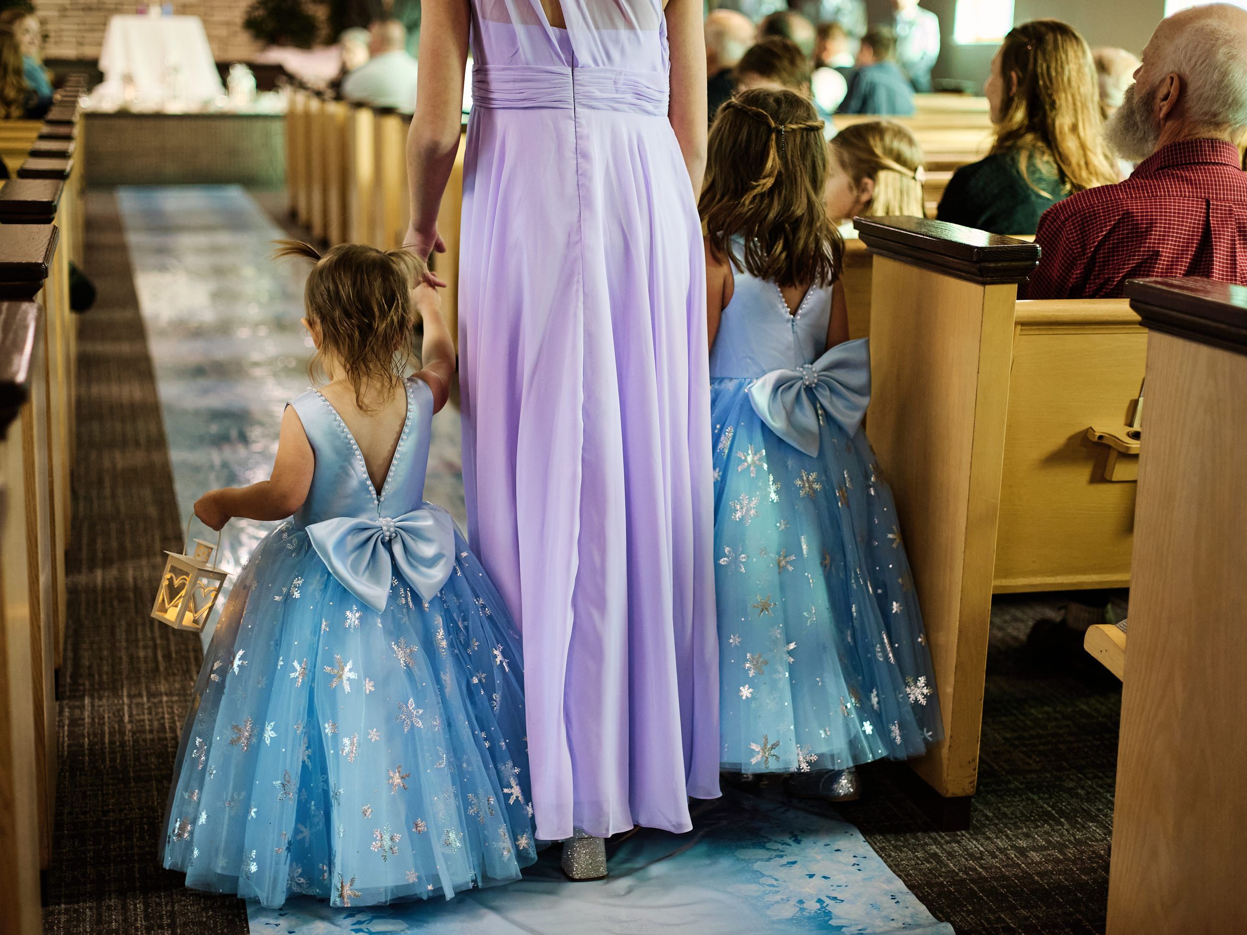 A row of bridesmaids in lavender and blue tulle dresses stand together at a wedding reception.