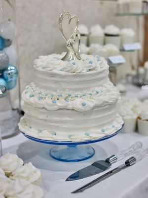 A white wedding cake with delicate blue decorative details sits on a blue glass pedestal cake stand.