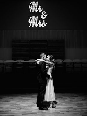 A couple performs an elegant ballroom dance in formal attire on a dark stage with dramatic lighting.