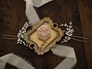 Vintage gold frame and pink ring box with delicate white baby's breath flowers on dark wooden surface.