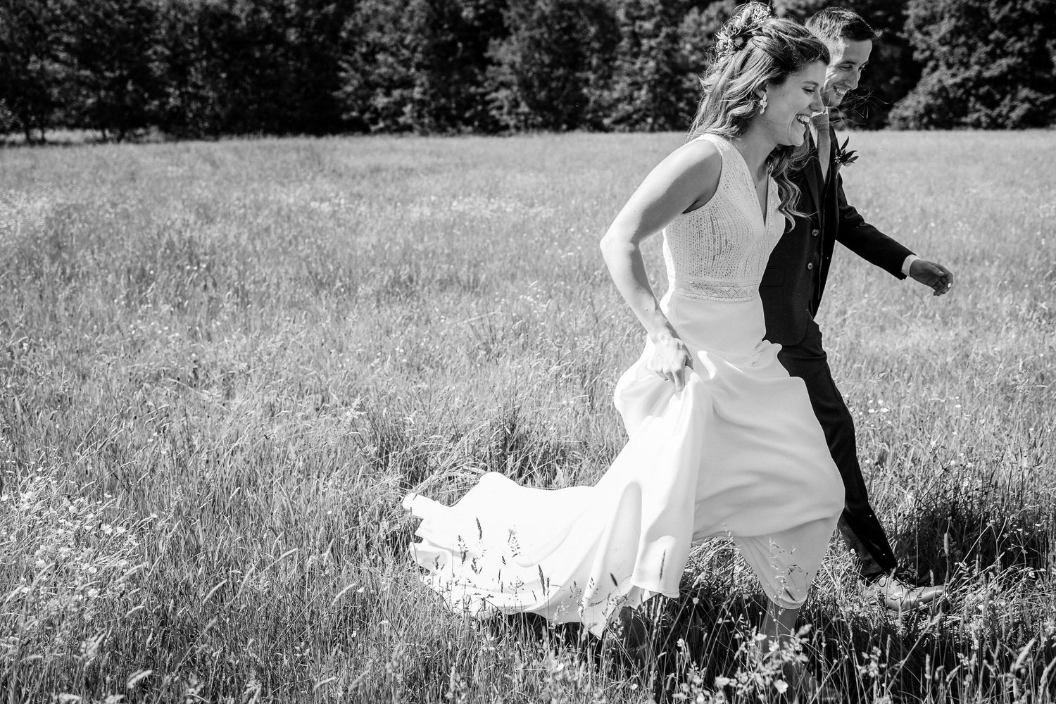 Couple in wedding attire walking along a wooded path covered in fallen autumn leaves.
