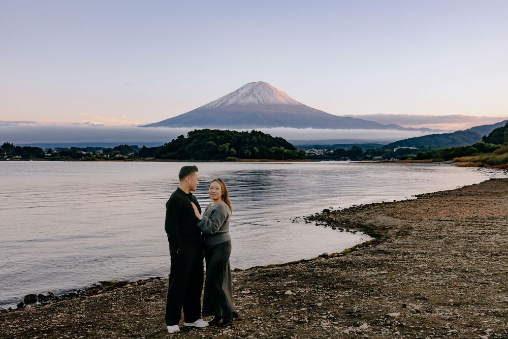 Mount Fuji rises majestically over a tranquil lake shore at sunset with its snow-capped peak reflecting in the water.
