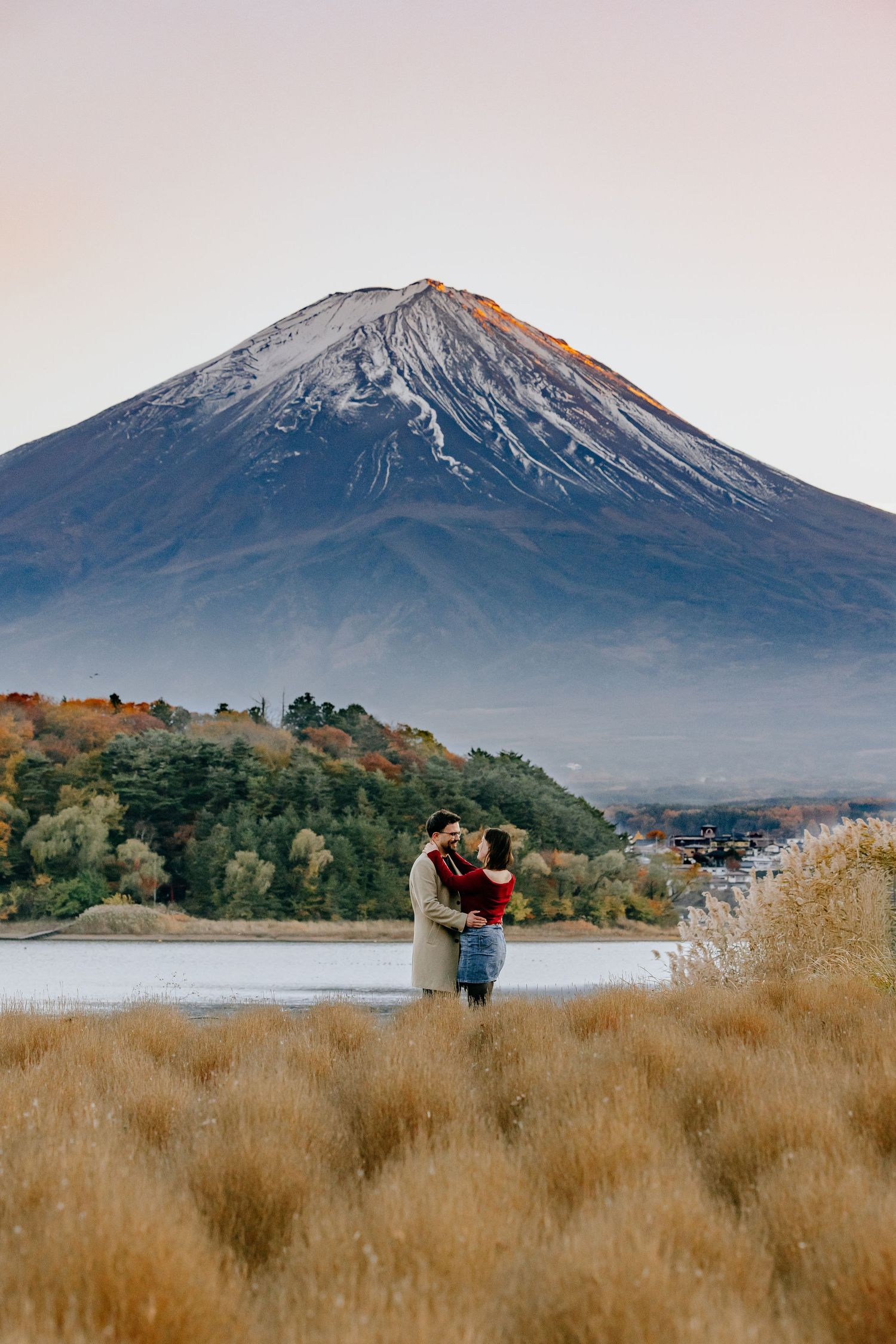 A couple embraces in a field of golden grass with Mount Fuji's snow-capped peak rising majestically in the background.